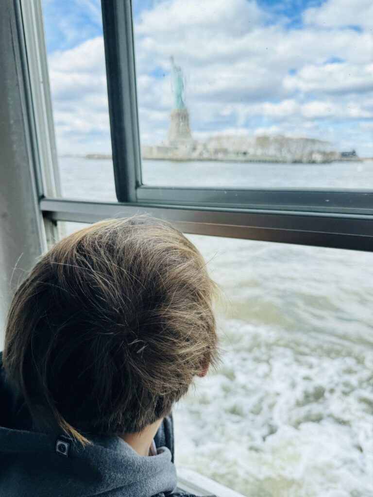 child looking out ferry at statue of liberty 